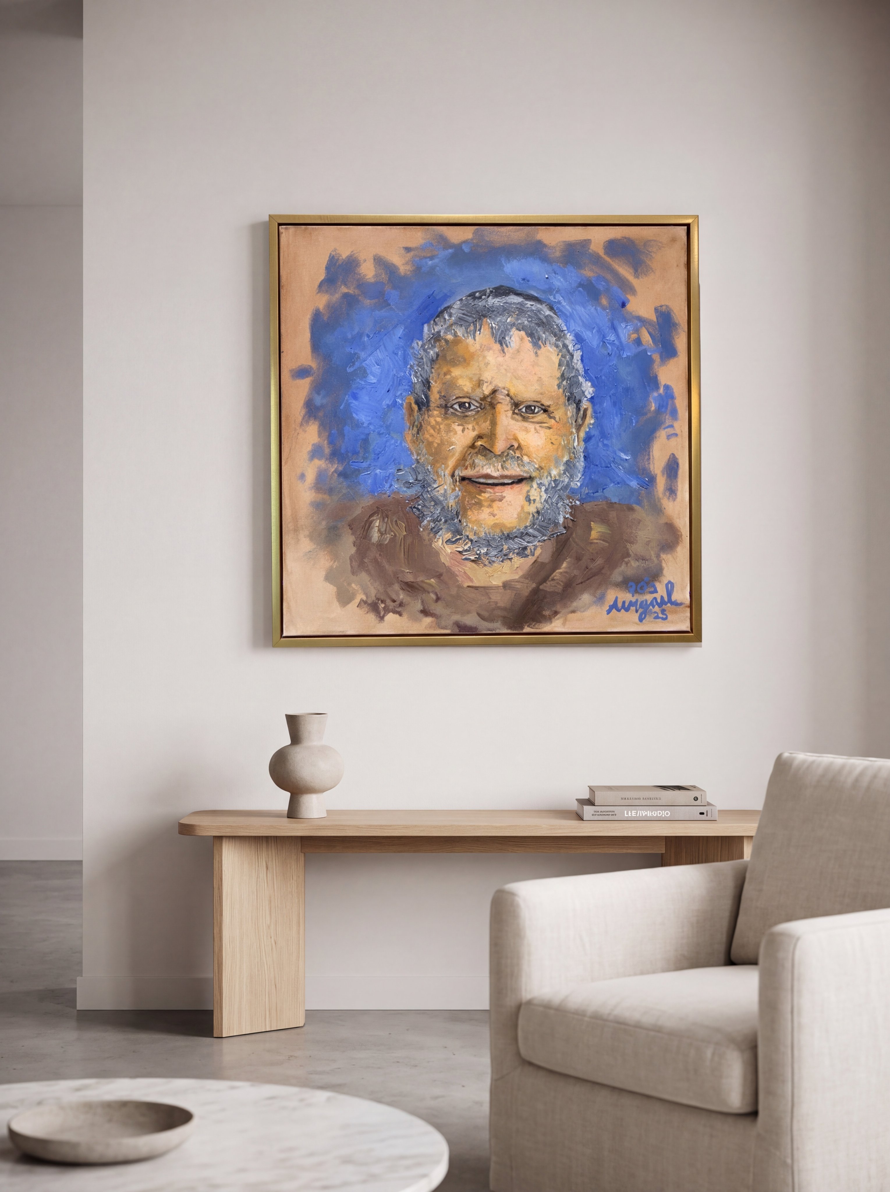 Framed oil portrait of a smiling bearded man against blue brushwork, displayed above a wooden console in a living room with a vase and armchair